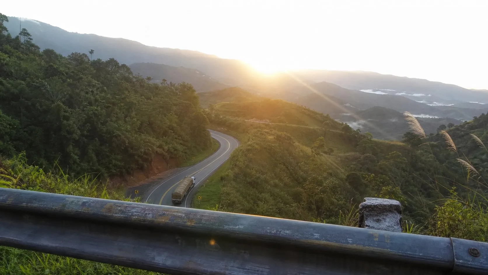 Rodovia de serra brasileira vista de um mirante no fim da tarde, com um caminhão descendo a curva ao longe